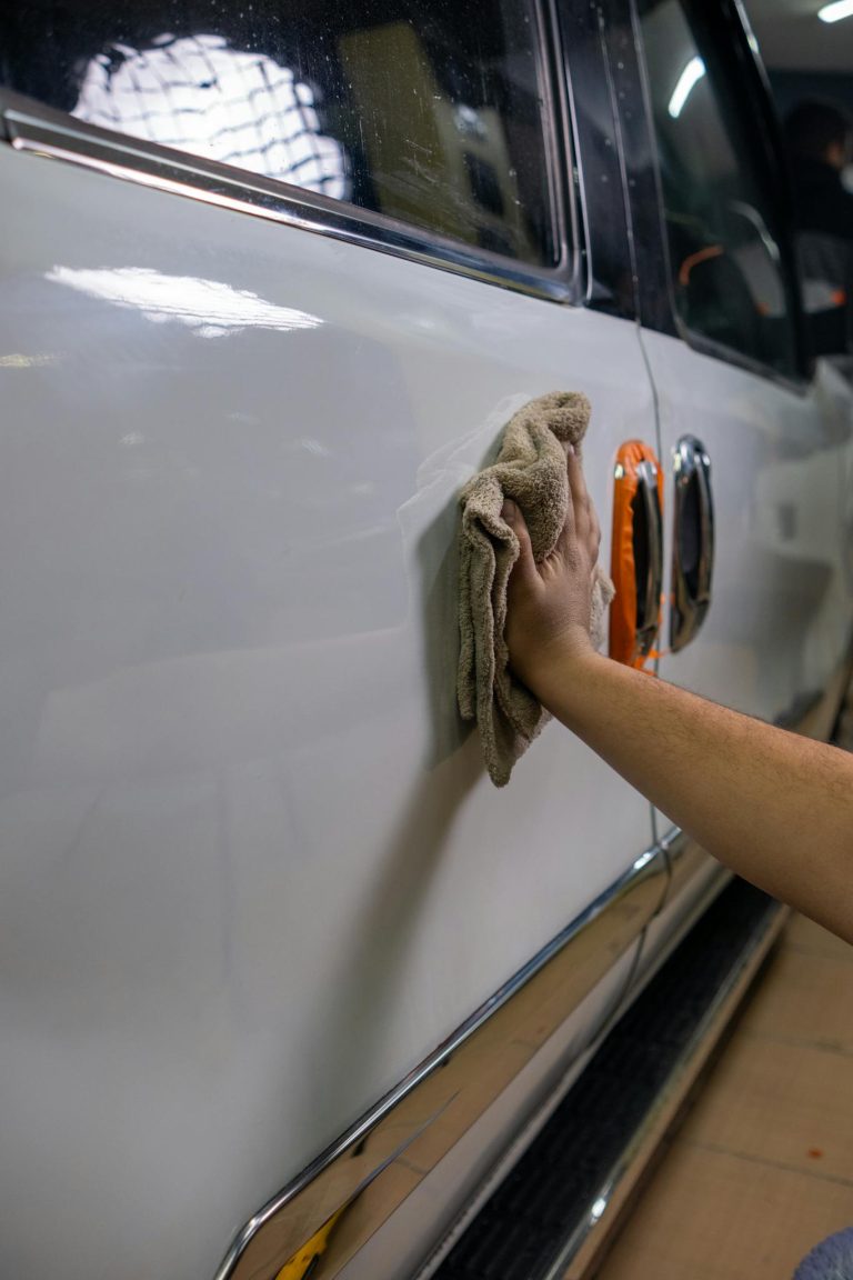 A person uses a cloth to polish the shiny surface of a car door indoors.
