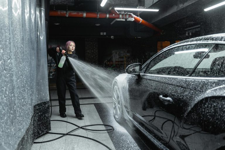 Woman using a pressure washer to clean a black car in an indoor car wash setting.